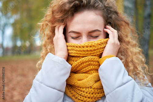 Redhead curly cheerful cute girl hiding her face with stylish yellow scarf
