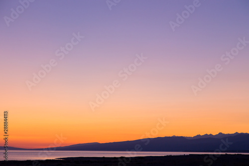 Dawn on a lake in the mountains. rays of the rising sun, orange color. Kyrgyzstan, Issyk-Kul Lake. Bright sky, background in warm colors. © Alwih