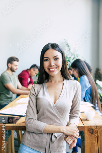 Happy young confident beautiful asian business woman in smart casual wear is posing on modern business team background. Co-workers. Start up team. Students together