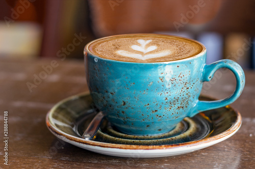 A cup of cappuccino with a leaf shape on the top over a wooden background  profile view.