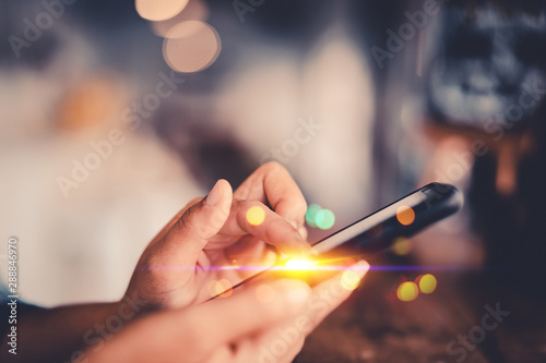 Woman hand using smart phone on old wood table texture background at coffee shop.