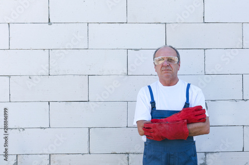 Construction worker wearing prfessional overalls and red protective gloves, standing near the white bricks wall photo