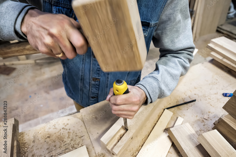 Man carpenter makes a hole in the wooden furniture detail with a hammer and chisel. Man carpenter makes a hole in the wooden furniture detail with a hammer and chisel.