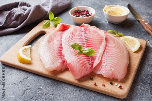 Raw fish fillet of tilapia on a cutting Board with lemon and spices. Dark table with copy space. photo