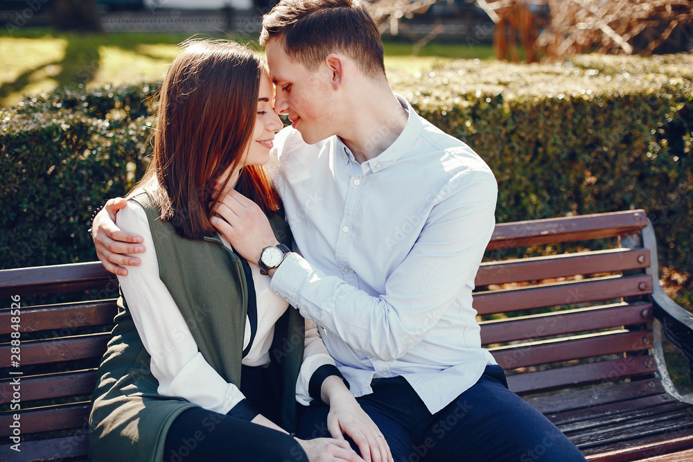handsome young guy in a blue shirt sitting on a bench in a sunny summer city along with her cute girl in a white shirt handsome young guy in a blue shirt sitting on a bench in a sunny summer city along with her cute girl in a white shirt