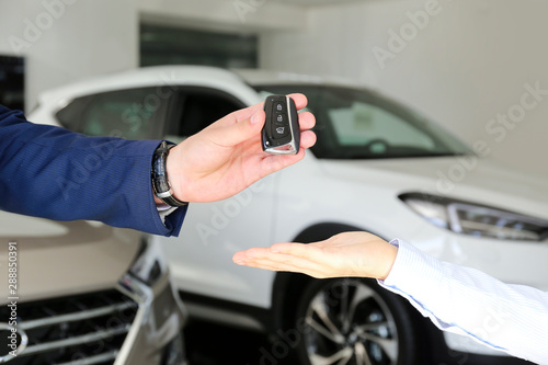 Car dealership sales person at work concept. Portrait of young sales representative wearing formal wear suit, showing vehicles at automobile exhibit center. Close up, copy space, background. © Evrymmnt