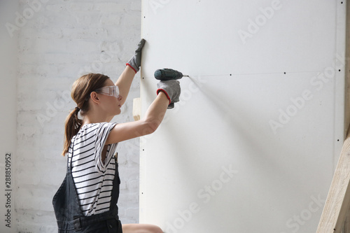 Young woman drilling screws into plasterboard with an electric screwdriver, home improvement concept photo