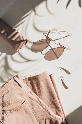Fashion composition with women's clothes and accessories on white background. Earrings, sunglasses, pink jean culottes on white background. Flat lay, top view lifestyle blog concept.