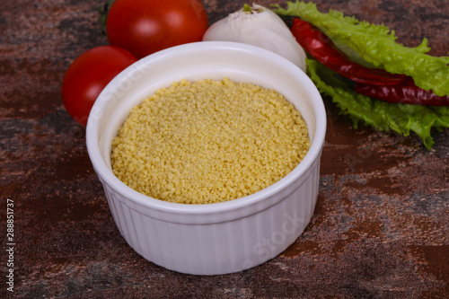 Raw couscous in the bowl served salad leaves, tomato and pepper photo