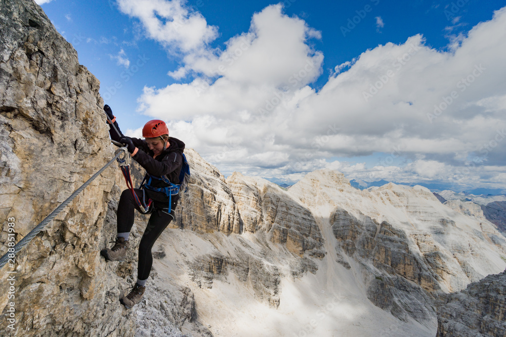 attractive brunette female climber on a steep and exposed Via Ferrata in the Dolomites
