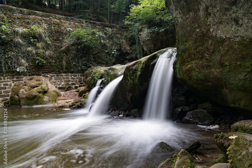 Fototapeta premium idyllic small waterfall in lush green forest landscape
