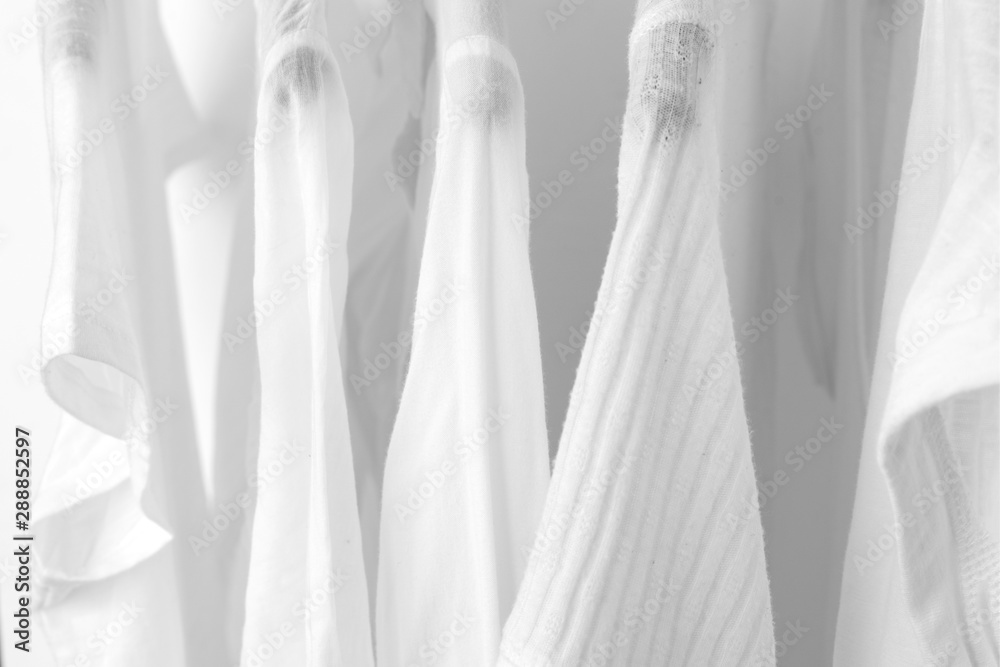 Row of white cotton clothes hang on black hangers on a rack in a shop. Woman minimalist wardrobe. Close-up. Row of white cotton clothes hang on black hangers on a rack in a shop. Woman minimalist wardrobe. Close-up.