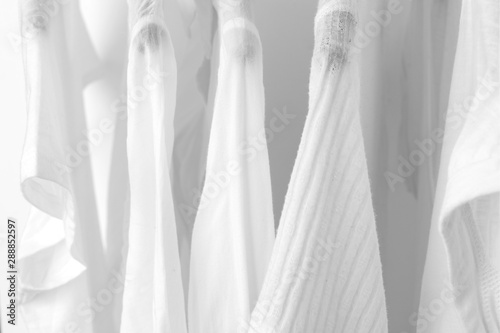 Row of white cotton clothes hang on black hangers on a rack in a shop. Woman minimalist wardrobe. Close-up.