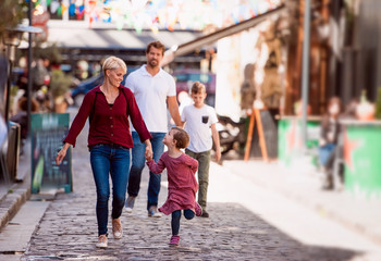 Young family with two small children walking outdoors in town on holiday.