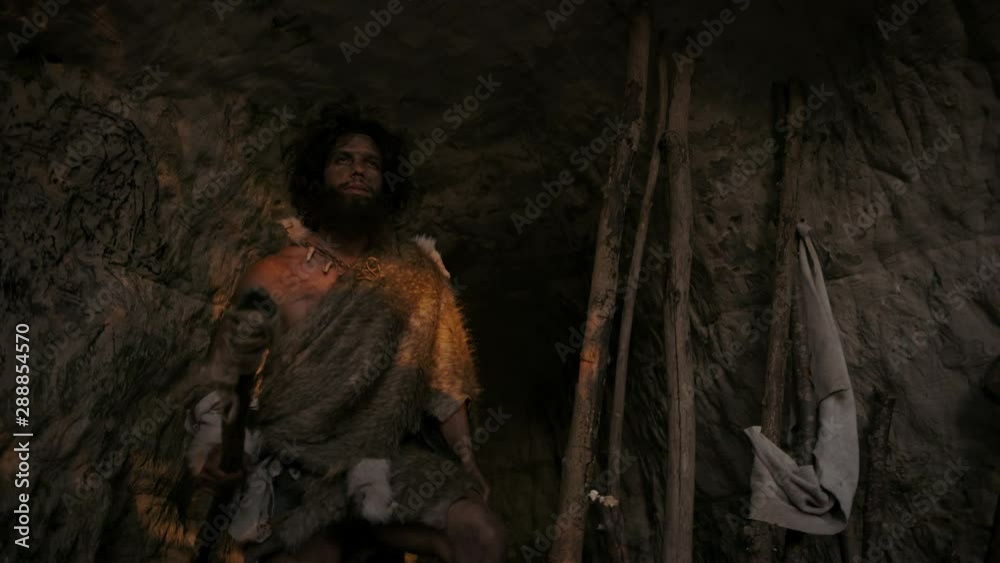 Portrait of Primeval Caveman Wearing Animal Skin Leaves Cave and Goes Hunting with a Stone Tipped Spear. Primitive Neanderthal Hunter / Homo Sapiens Squints at the Sun Walking out of Den. Tilt Up Shot Portrait of Primeval Caveman Wearing Animal Skin Leaves Cave and Goes Hunting with a Stone Tipped Spear. Primitive Neanderthal Hunter / Homo Sapiens Squints at the Sun Walking out of Den. Tilt Up Shot