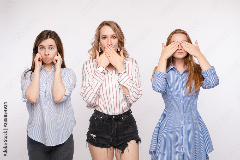 Three young woman friend posing with closing eyes ears and mouth looking at camera medium shot. Stylish female having fun hiding sensory organs isolated at white studio background