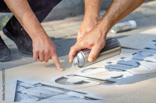 Hand holds an aerosol spray can, puts the image on the asphalt through a stencil