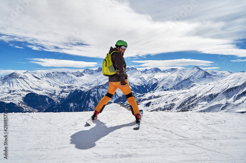 Obraz na płótnie Man skier smiling and posing with a beautiful winter mountain panorama in Les Sybelles ski domain, France, on a sunny day with blue sky and white clouds. w salonie