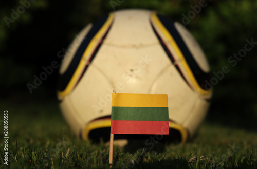 Lithuanian flag who is created from three lines yellow, green and red. World Championship 2022. Euro 2020. National flag on wooden stick with soccer ball in background photo