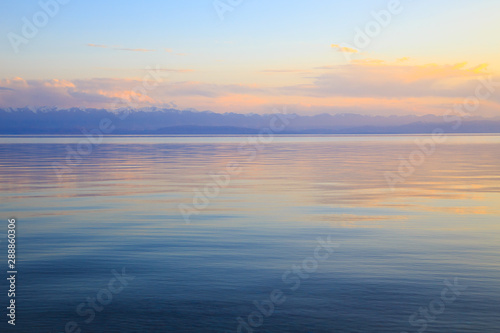 Beautiful sunset on a lake in the mountains. Kyrgyzstan, Issyk-Kul Lake. Bright sky, background in warm colors.