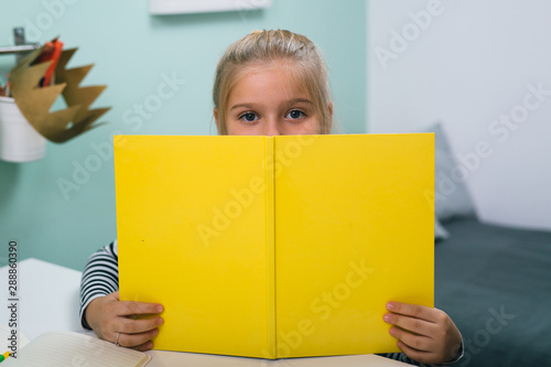 little girl peeking behind yellow book at her home