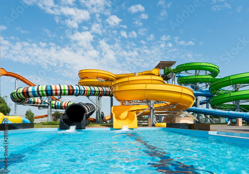 Fototapeta Naklejka Na Ścianę i Meble -  Water park, bright multi-colored slides with a pool. A water park without people on a summer day with a beautiful, cloudy blue sky