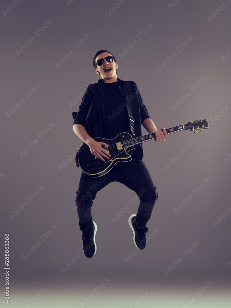 Naklejka premium Fifteen years old guitarist with a black electric guitar. Teenage musician holds guitar