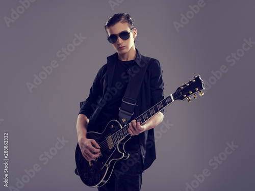Fifteen years old guitarist with a black electric guitar. Teenage musician holds guitar