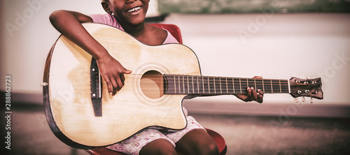 Portrait of smiling schoolgirl playing guitar in classroom