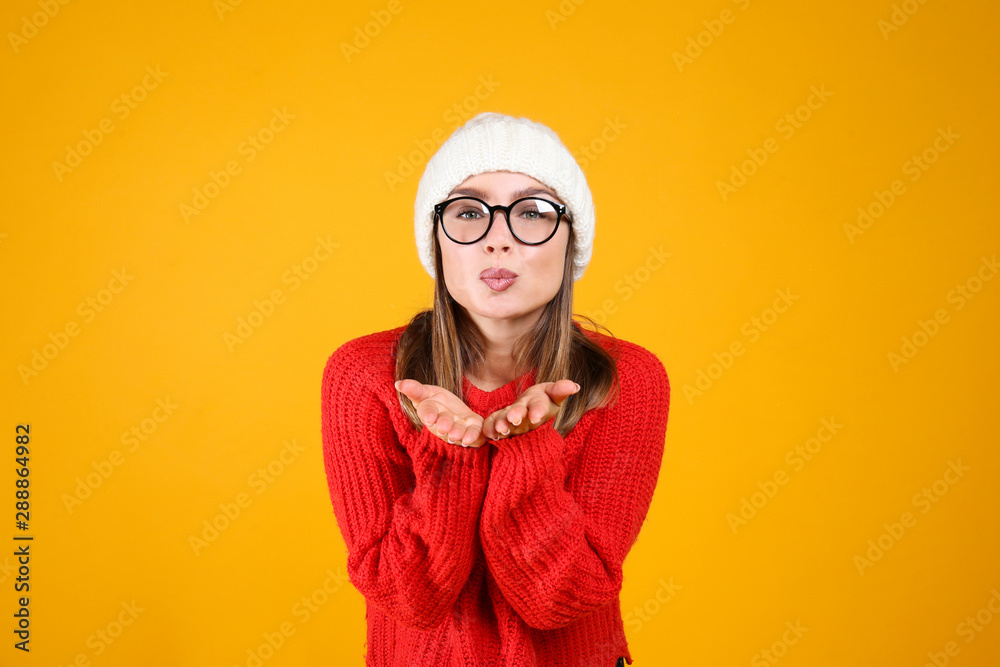 Close up portrait of a young beautiful woman with light make up on, wearing knitted sweater & blue woolen beanie. Attractive female in winter knitwear outfit, isolated on yellow background. Copy space