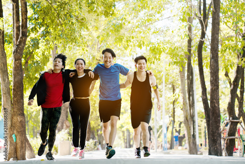 Group of Asian runners, men and women, jogging in park in the morning of summer. With fresh green trees Providing clean oxygen And has benefits for people body Exercising daily makes your body healthy