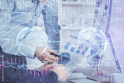 Double exposure of chart with businessman typing on computer in office on background. Concept of hard work.