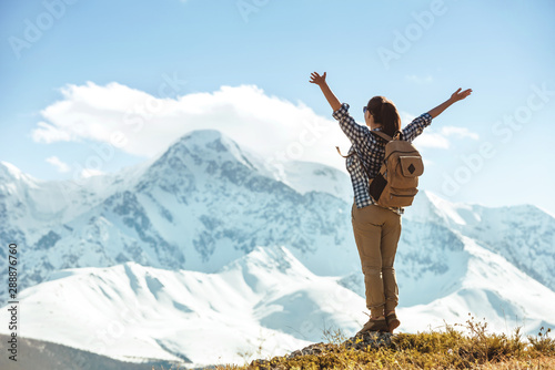 Happy lady hiker stands with raised arms against mountains