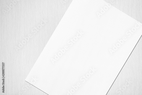 Close up of empty white rectangle poster or card mockup lying diagonally with soft shadow on neutral light grey textured background. Flat lay, top view. Open composition.