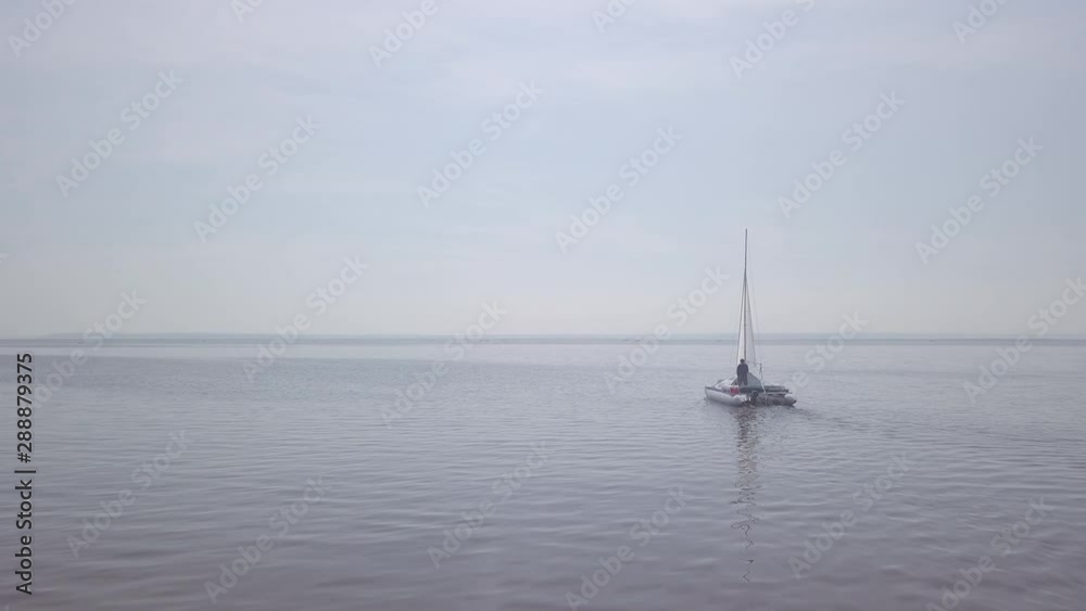 Young man motorsailing the small catamaran on the lake at light wind. Camera approaches and orbits. Original clip without color grading. Shot on DJI Mavic Pro in D-Log profile. Young man motorsailing the small catamaran on the lake at light wind. Camera approaches and orbits. Original clip without color grading. Shot on DJI Mavic Pro in D-Log profile.