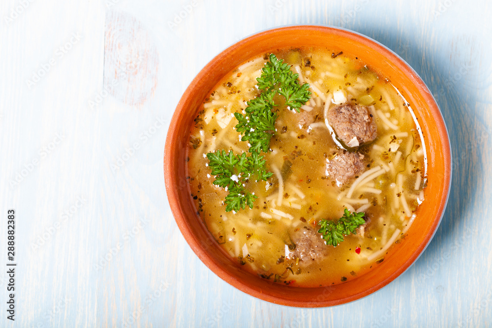 Homemade soup with noodles and meatballs on a wooden table. Traditional rural dinner