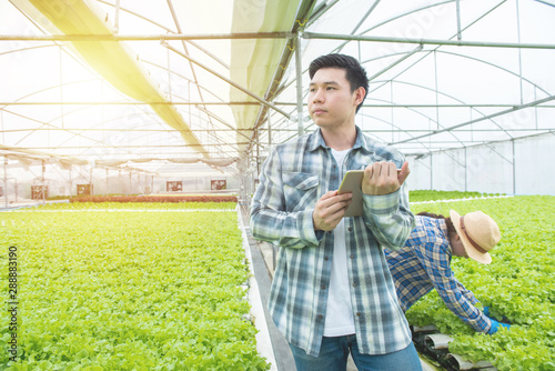 Portrait of young asian professional farmer man hand hold tablet with asian woman coworker working in greenhouse hydroponic organic farm,Technology and small business entrepreneur concept