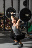 Strong female weight lifter doing snatch with heavy barbell in gym.