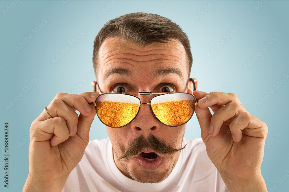 Φωτογραφία Oktoberfest man with sunglasses full of light beer, looking at sea or ocean of alcohol on blue background