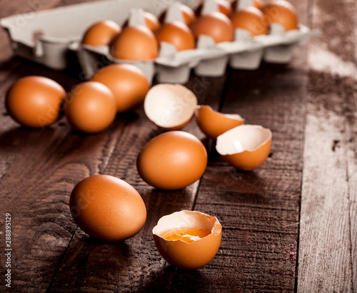 Brown eggs in a box and broken egg with yolk on rustic table.