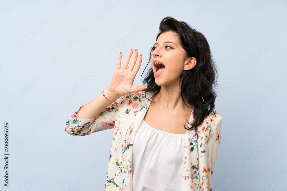 Young woman over isolated blue background shouting with mouth wide open Young woman over isolated blue background shouting with mouth wide open