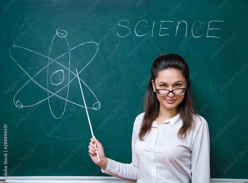 young teacher with glasses talks about science near blackboard