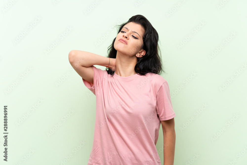 Young woman over isolated green background with neckache Young woman over isolated green background with neckache