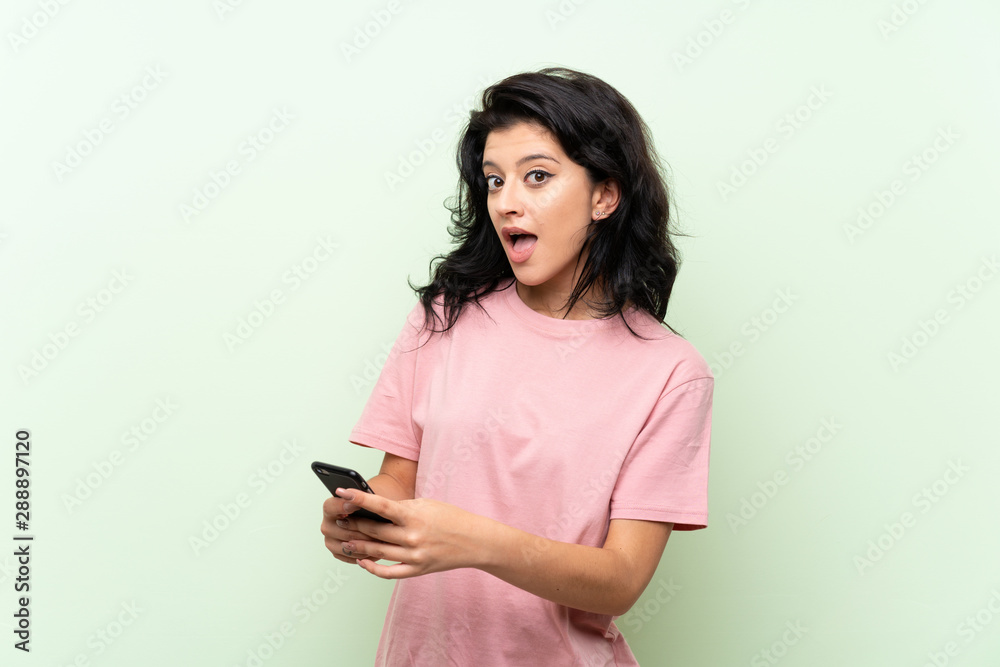 Young woman over isolated green background surprised and sending a message Young woman over isolated green background surprised and sending a message