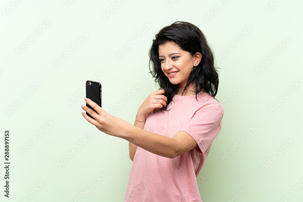 Fototapeta premium Young woman over isolated green background making a selfie