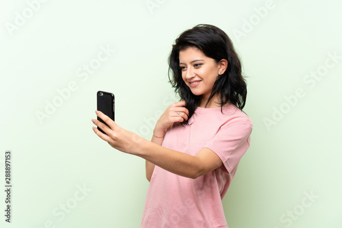 Young woman over isolated green background making a selfie