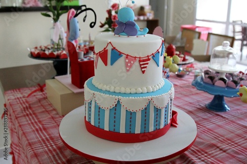  Blue and white cake with red details on a table. Party environment with candies and several ornaments.