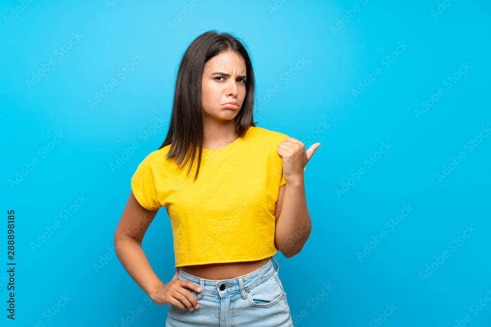 Young girl over isolated blue background unhappy and pointing to the side Young girl over isolated blue background unhappy and pointing to the side