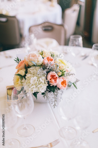 Fine wedding floral arrangement with pink peonies, white roses, dusty miller, and greenery, silver vase, white tablecloth, luxury wedding reception decor