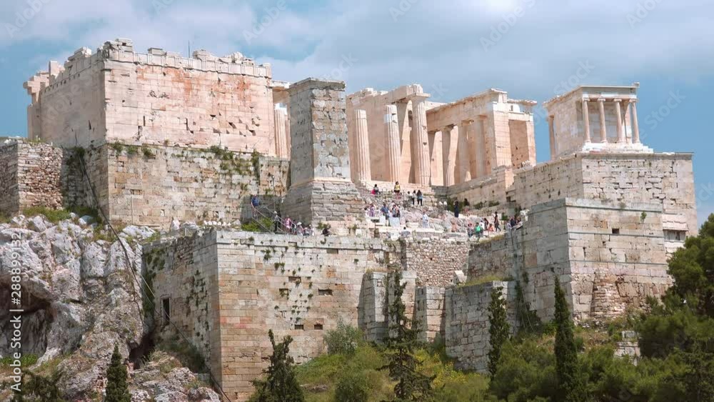 Tourists walking around the Acropolis of Athens. Icon of the hellenic civilization, Parthenon. Picturesque view of antique marble ruins on hill. Mediterranean plants near famous historical temple Tourists walking around the Acropolis of Athens. Icon of the hellenic civilization, Parthenon. Picturesque view of antique marble ruins on hill. Mediterranean plants near famous historical temple